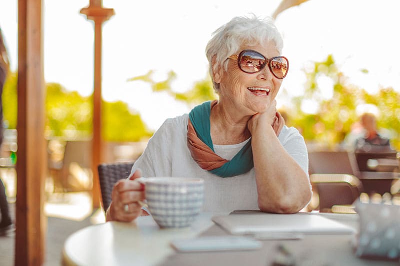 senior woman in sunglasses having coffee outside