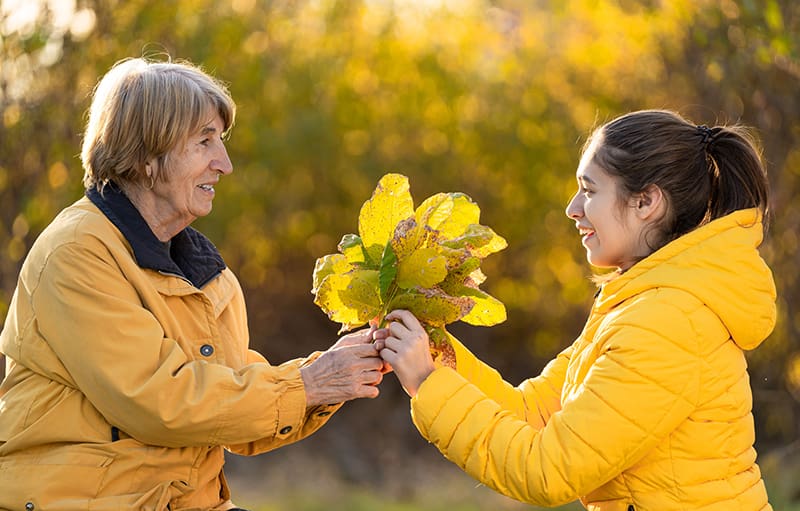 Smiling grandmother giving a bouquet of yellow flowers to her teenage granddaughter. Both wearing yellow jackets.
